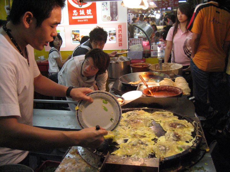 士林夜市の屋台で、鉄板の上の蚵仔煎を返す焼き手