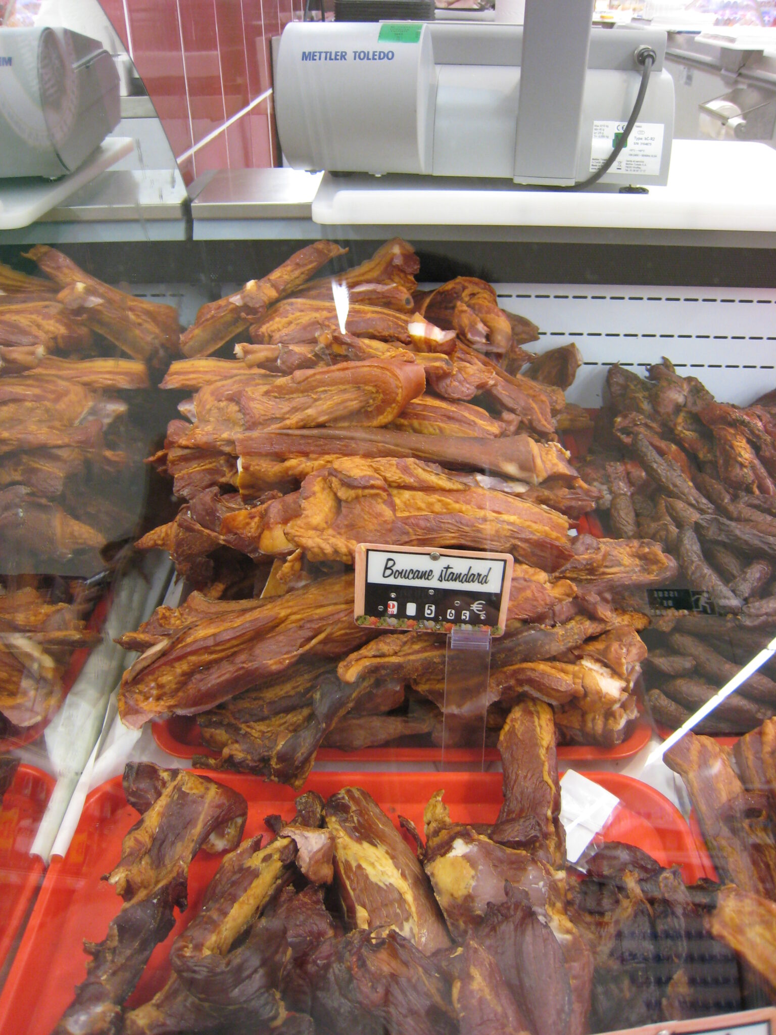値札を添えて店頭に吊るされたブカネ（燻製豚バラ）