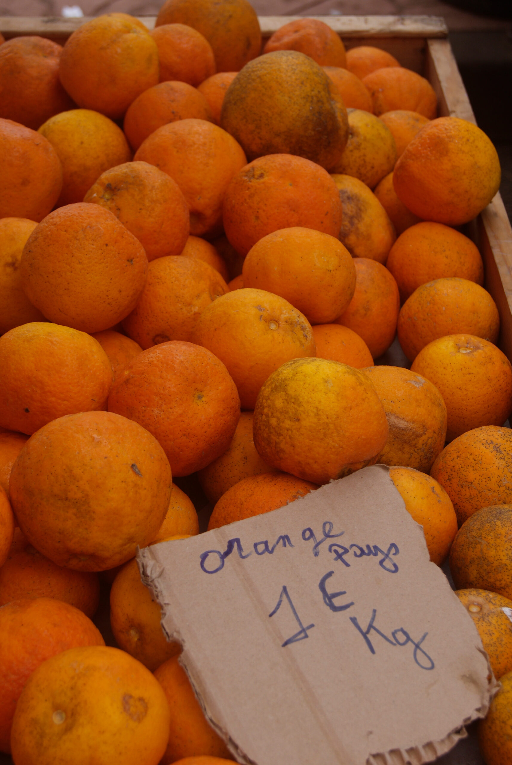 「oranges pays 1€ kg」の札を立てたオレンジの山