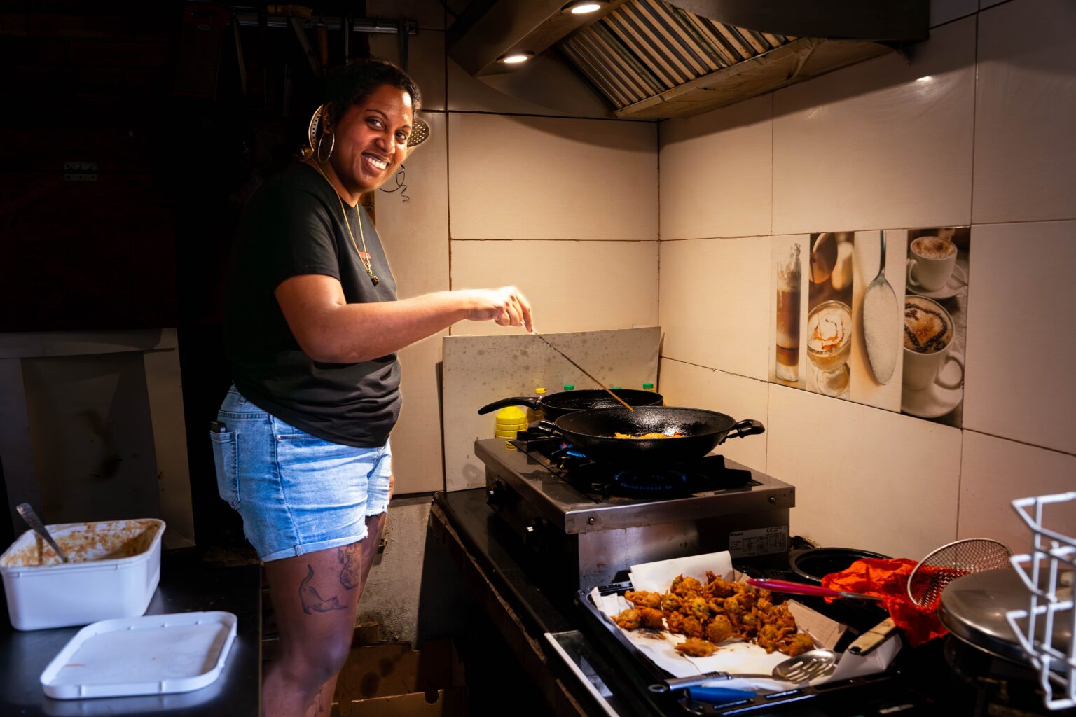厨房のコンロで揚げ物を返す女性と、手前に並ぶ揚がったばかりの具