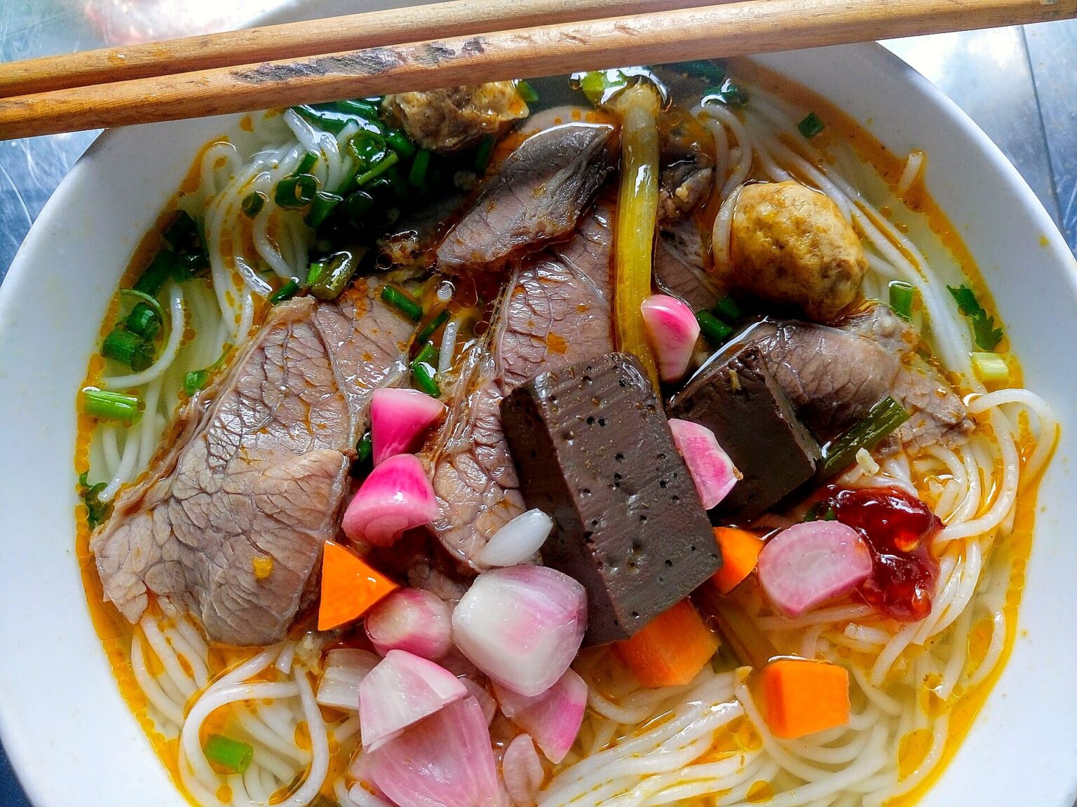丸い米麺の上に牛すね肉、豚の血の煮こごり、練りもの、レモングラス、酢漬けの赤玉ねぎ。ダナンで撮影