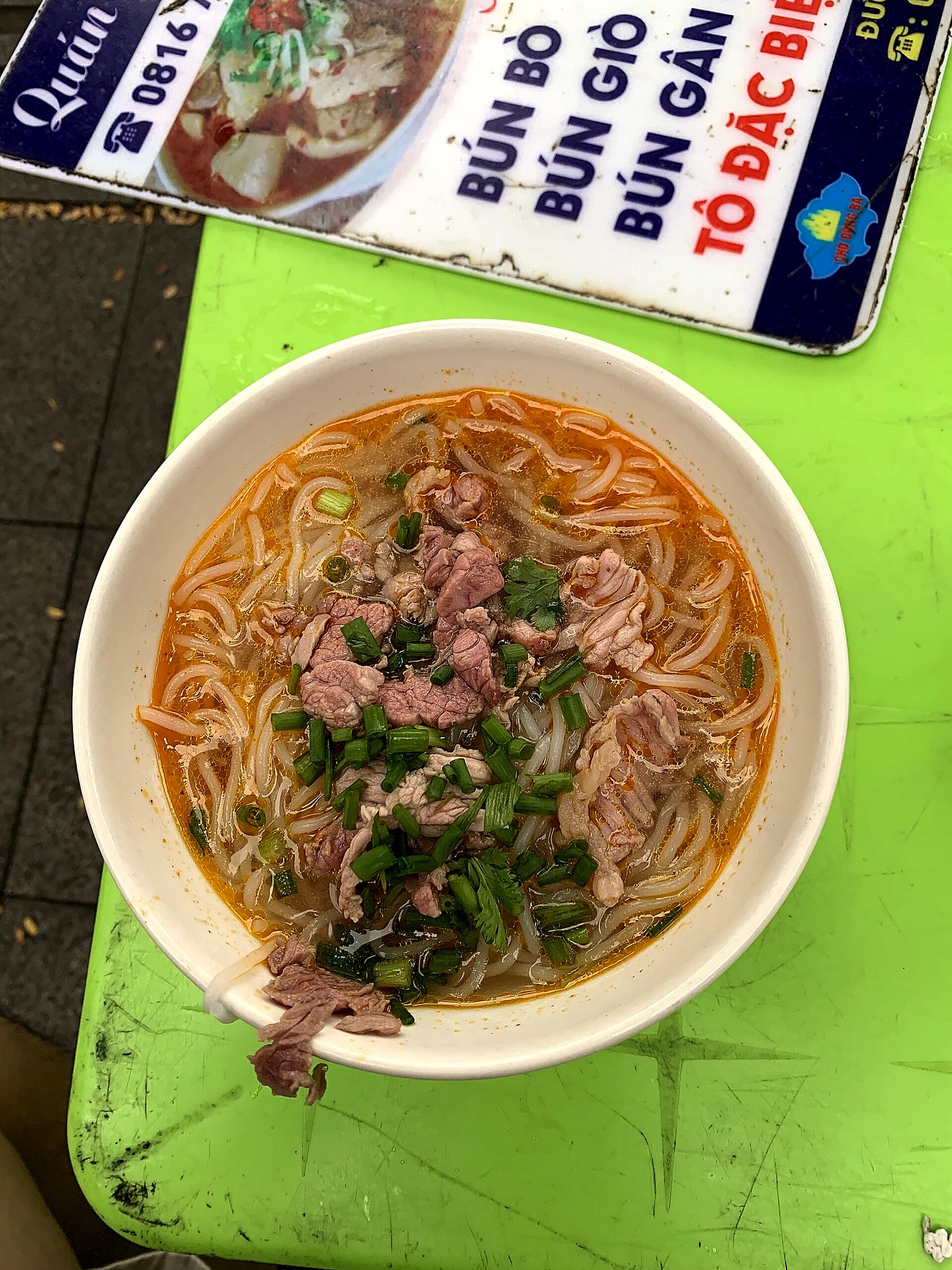緑色の卓の上に丼。奥にBÚN BÒ／BÚN GIÒ／BÚN GÂNと書かれた店の札