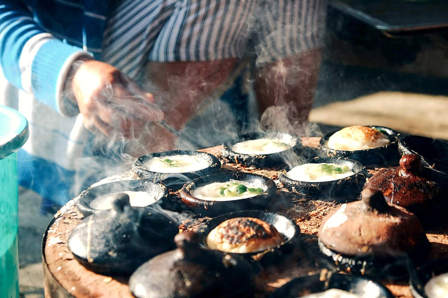いくつも並んだくぼみの型から煙が立ちのぼる、路上の焼き台