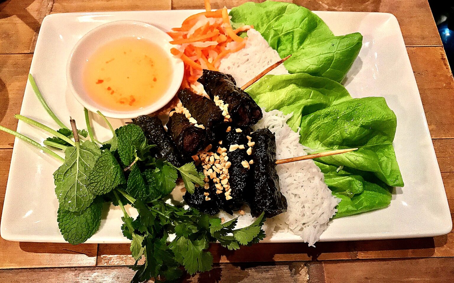 白い角皿に葉巻きの肉、レタス、香草、なます、細い麺、たれの椀。イギリス・マンチェスターの店で撮影