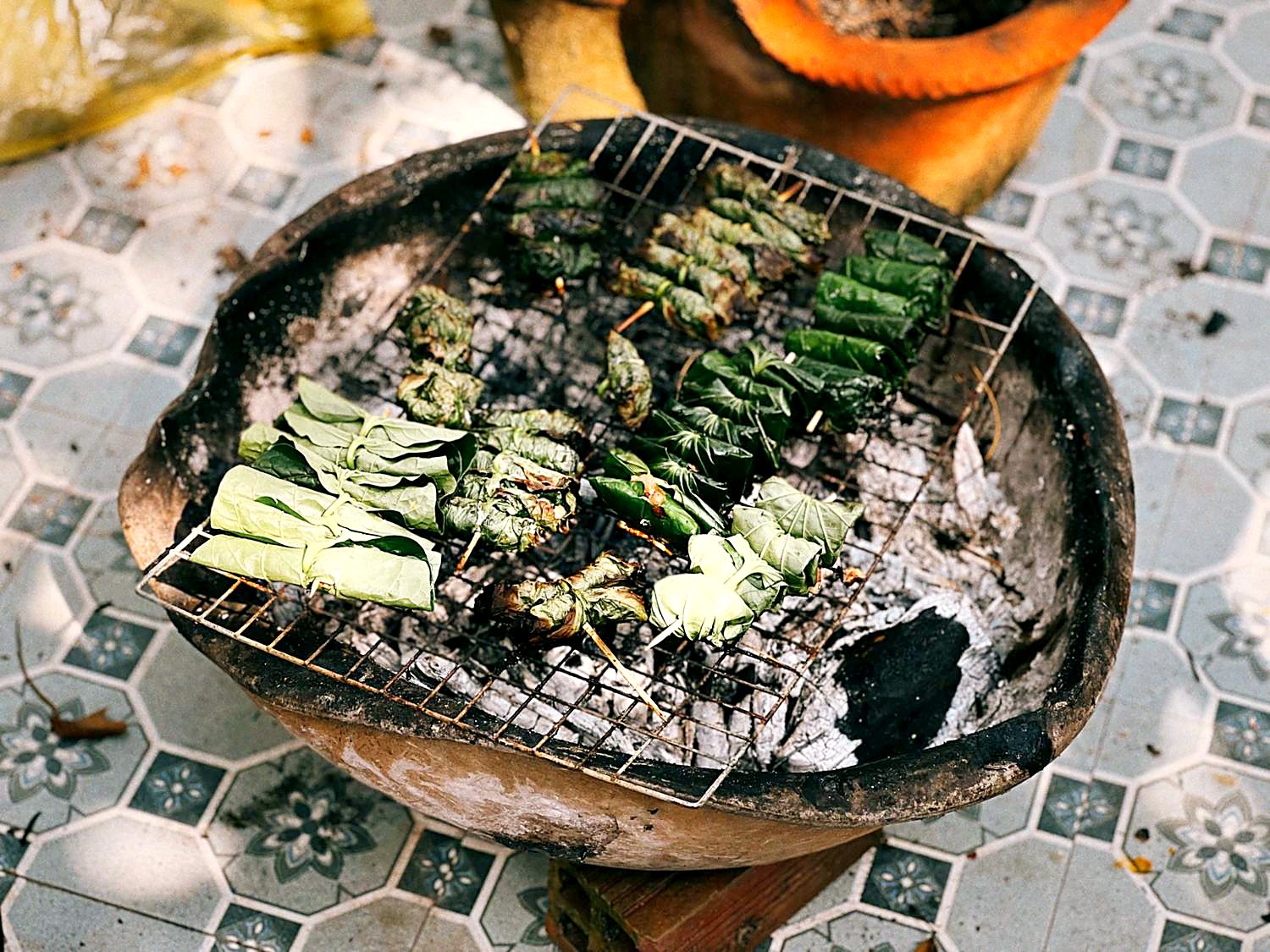 タイルの上に置いた炭の焼き台。金網の上で葉巻きの串が焼かれている