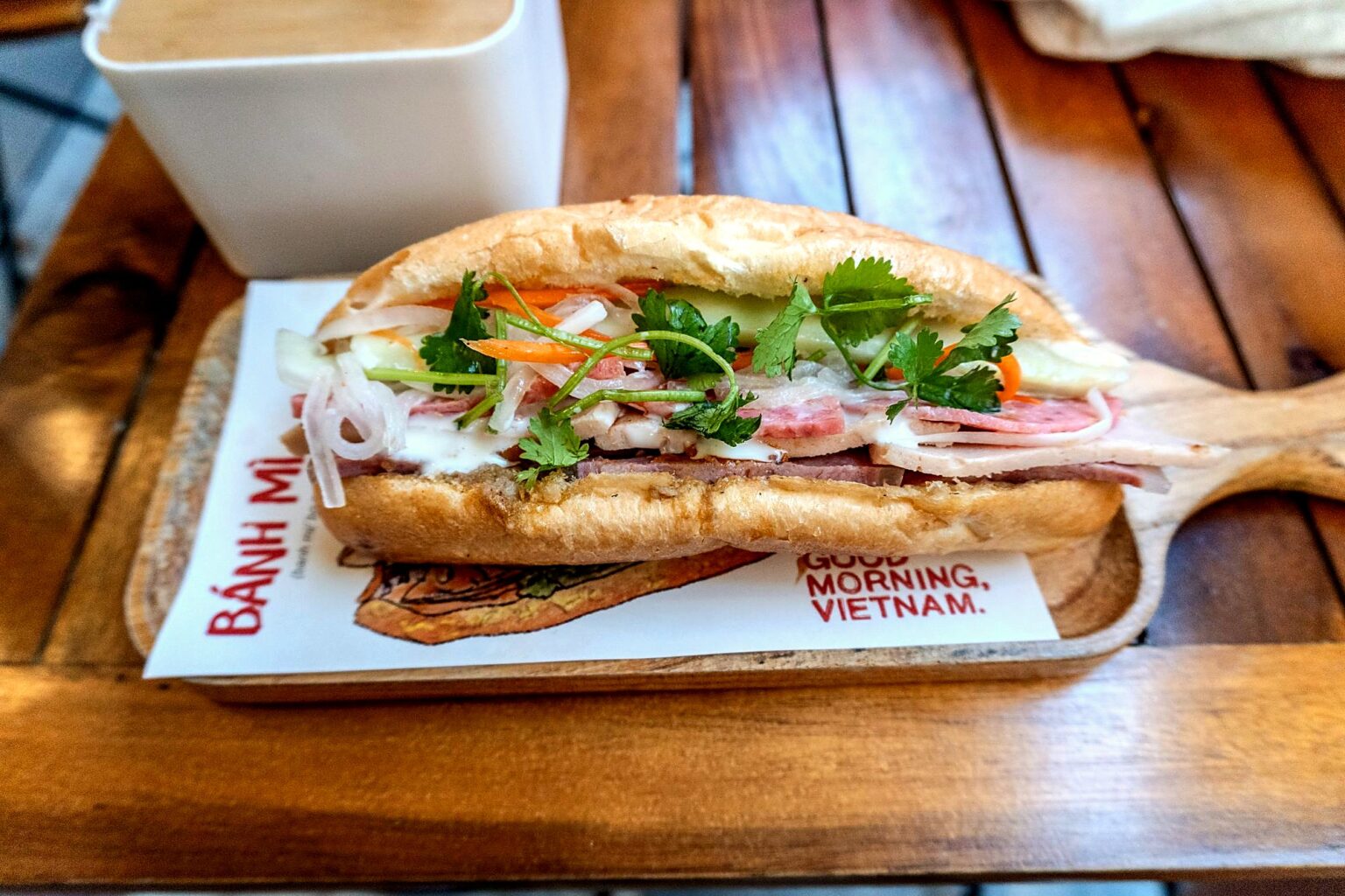 「BÁNH MÌ」と刷られた紙の上、具の見える開いたバインミー