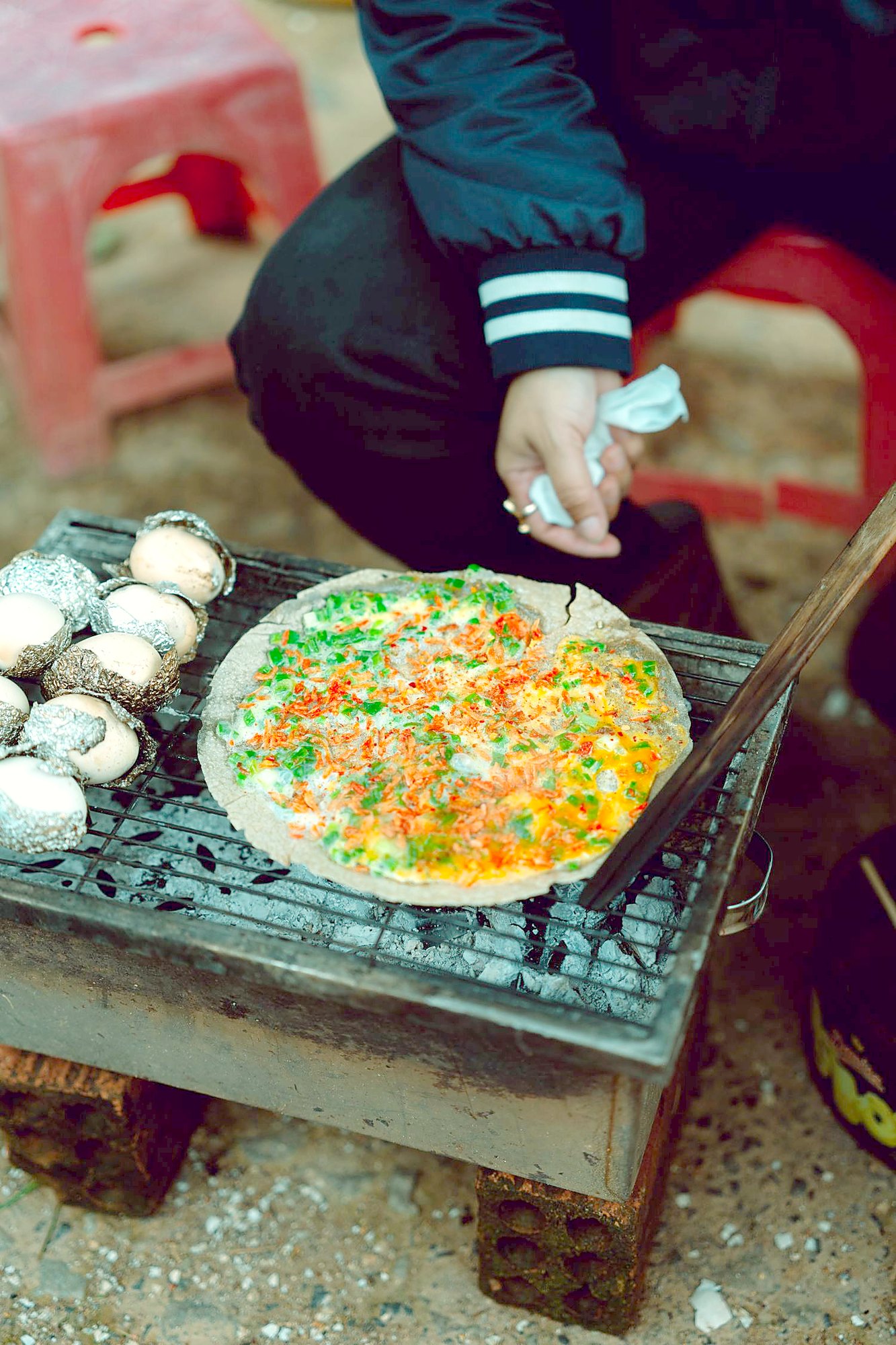 小さな炭の焼き台の上で、丸いライスペーパーに卵と赤や緑の具が広げられている