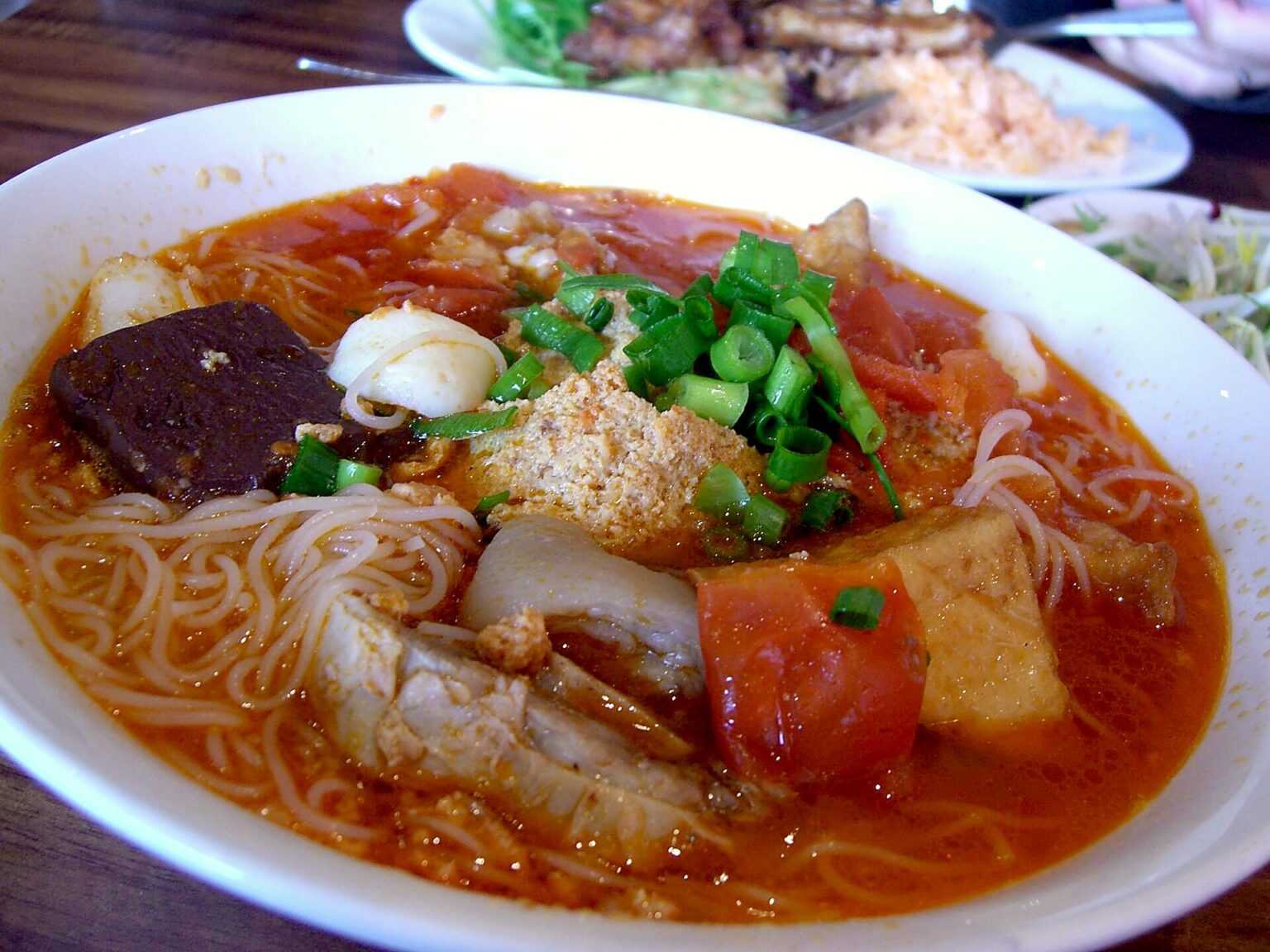 白い丼に細い米麺、蟹のそぼろ、豚の血の煮こごり、揚げ豆腐、トマト、豚肉、青ねぎ