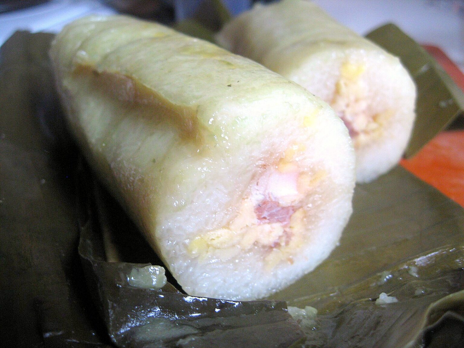 円筒形のもち米の塊の切り口。中に緑豆の餡と豚の脂身が見える。下にバナナの葉