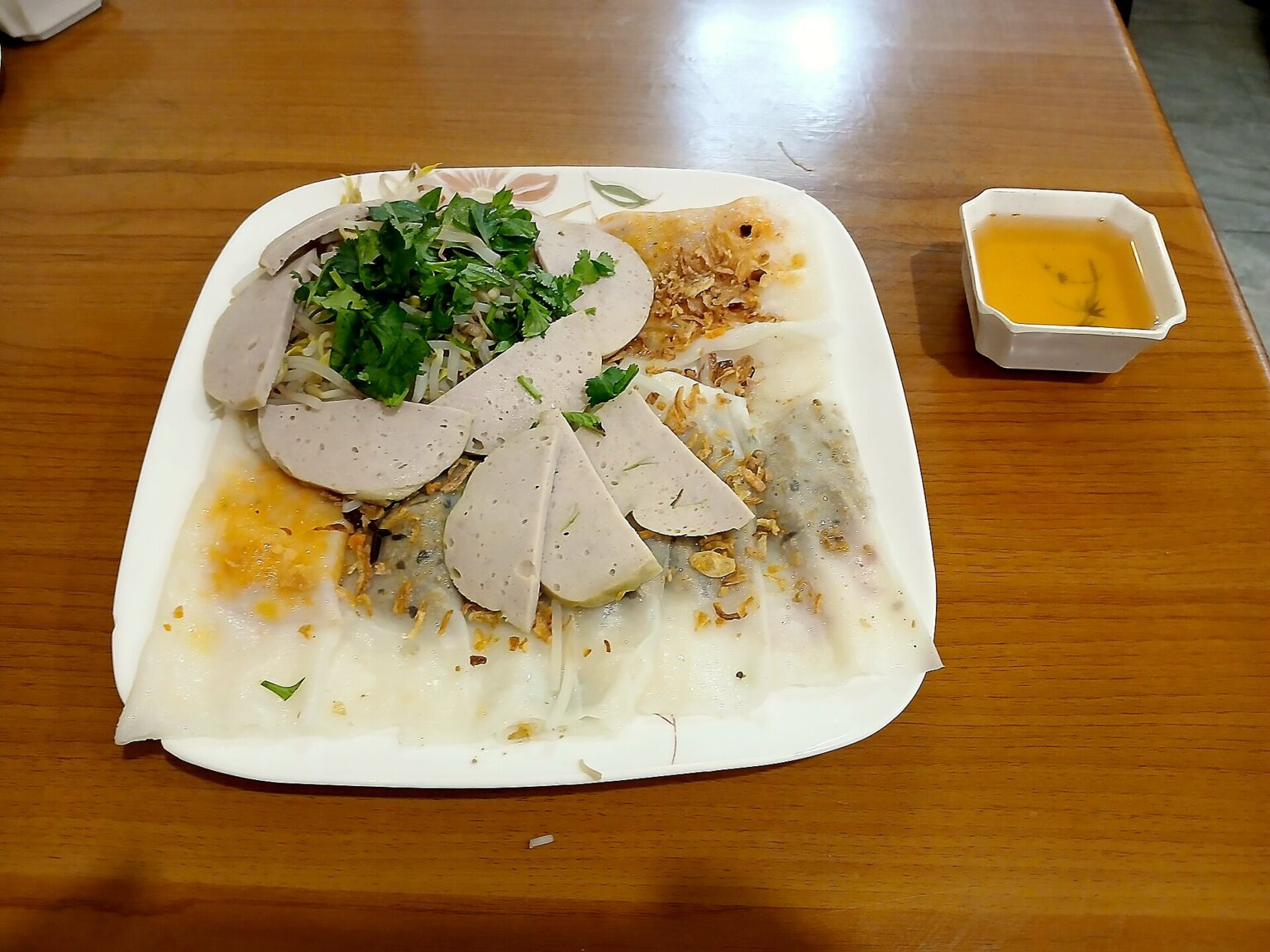 白い角皿に肉を包んだ巻きものとチャールア（練りもの）の薄切り、香草。となりに黄色いたれ