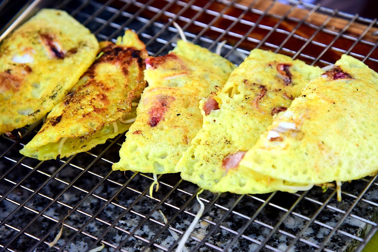 焼き網の上に並んだ、半分に折った黄色いバインセオ