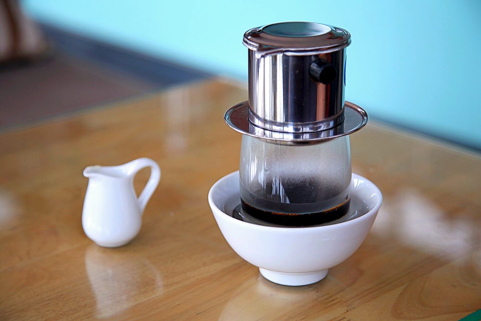 白い器の上に置かれたフィンから、コーヒーが落ちている。左にミルクピッチャー