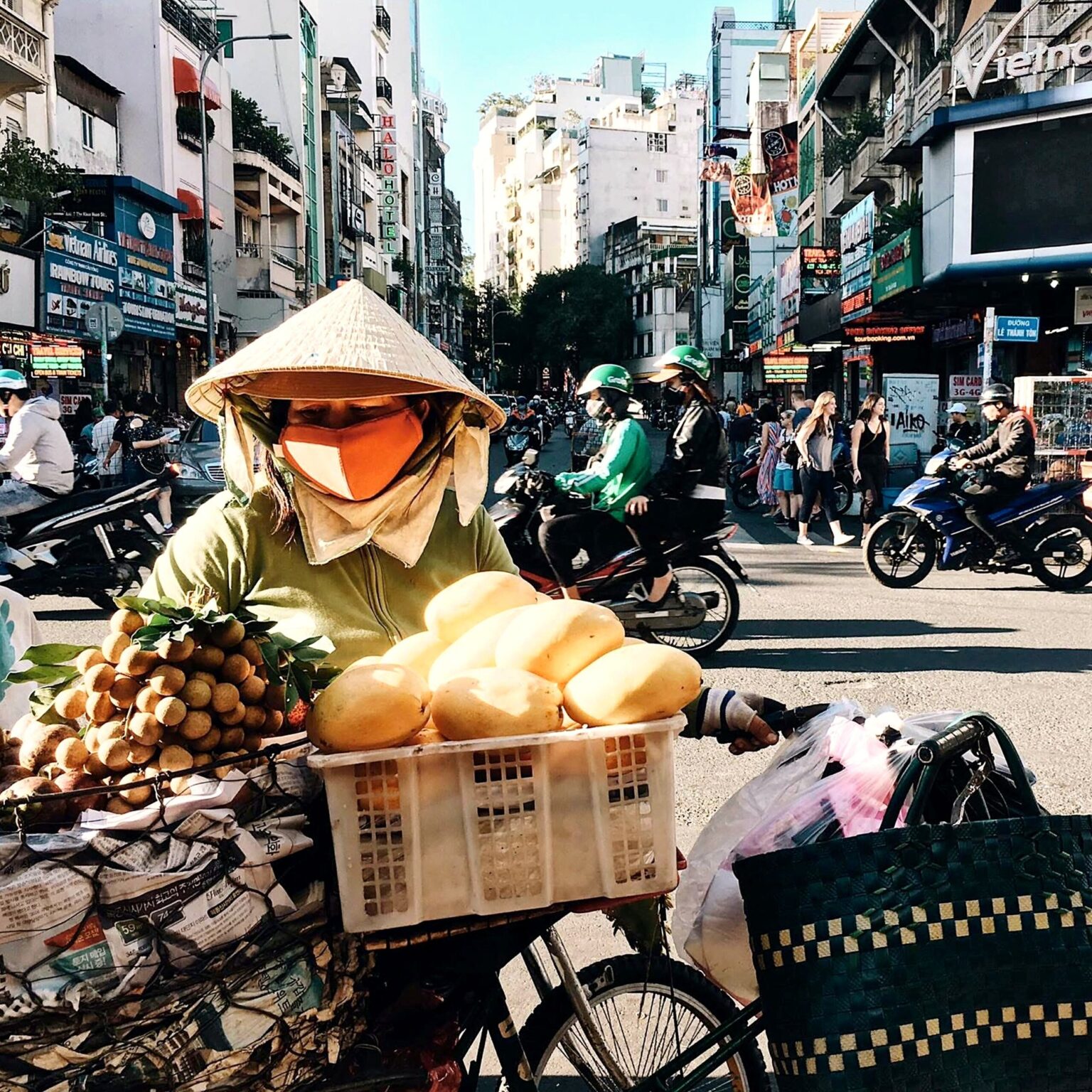 自転車の荷台にパンと果物を積んで売る笠の女性