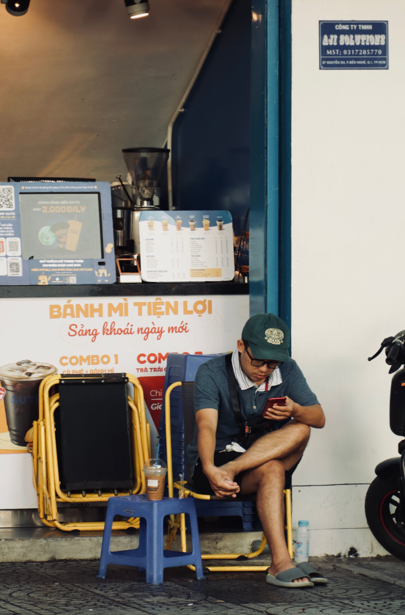 bánh mìの小さな店の前、青い椅子に座る男性