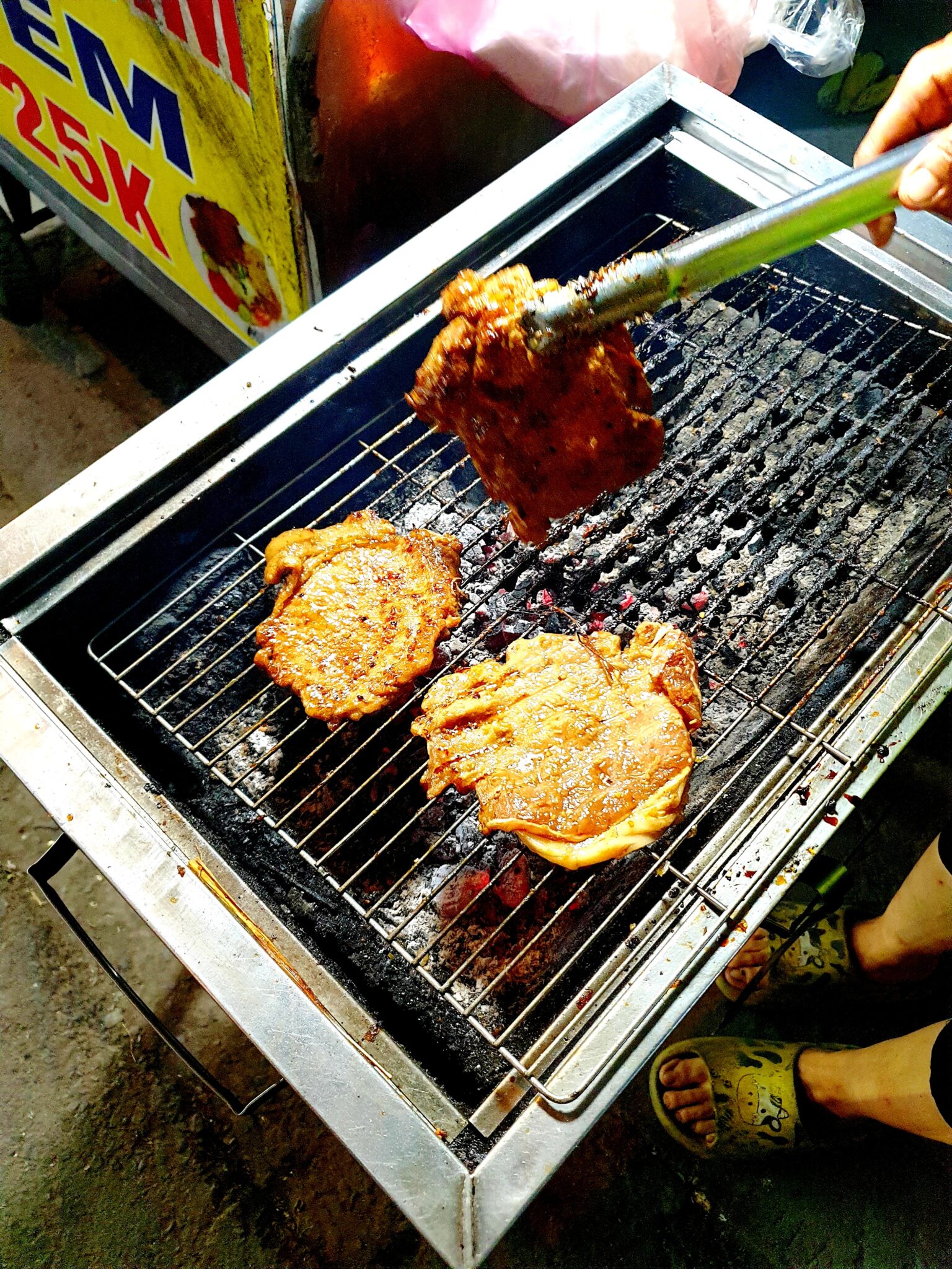 炭火の網の上の焼き豚。トングで返す手元
