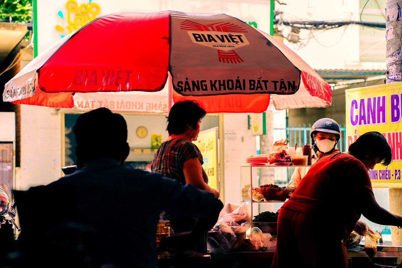 赤いBia Việtの傘の下で食べる人々の屋台