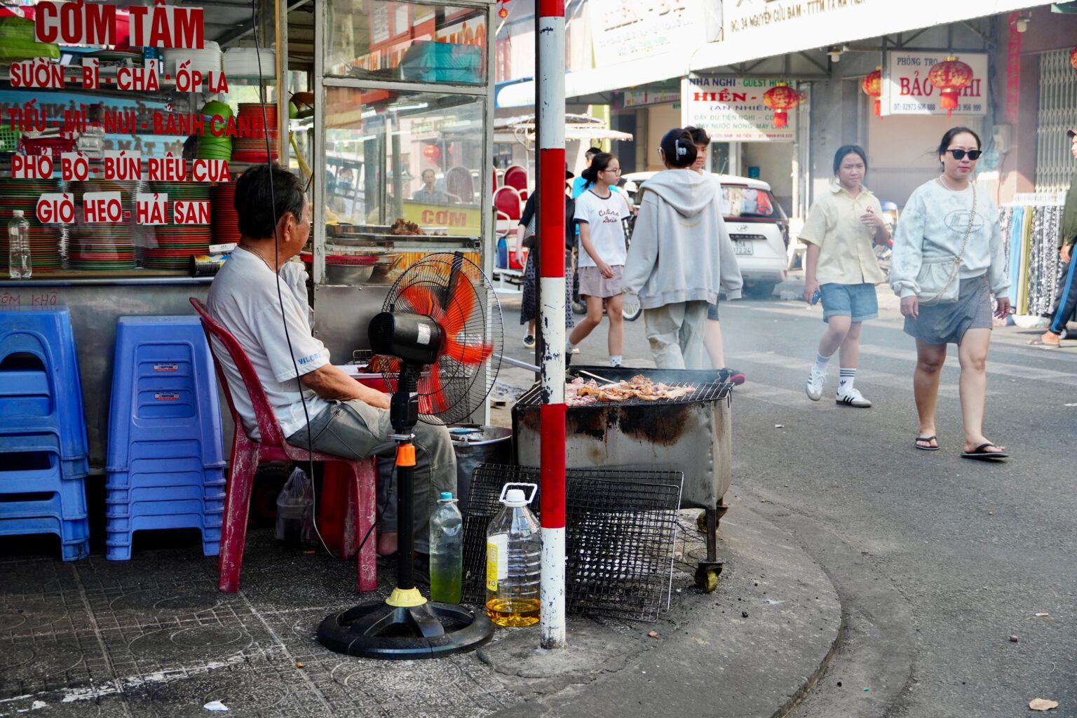 「CƠM TẤM」の看板の路上店。炭火の網と青い椅子