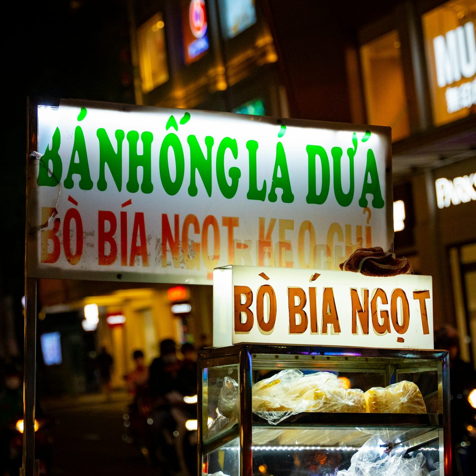 夜のストリートフードカート。電飾看板（bánh hồng lá dứa／bò bía ngọt＝菓子類の屋台）