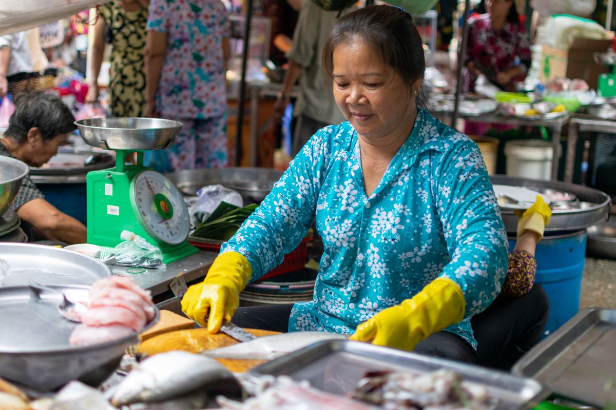 市場で黄色い手袋をして魚を売る青い服の女性、秤