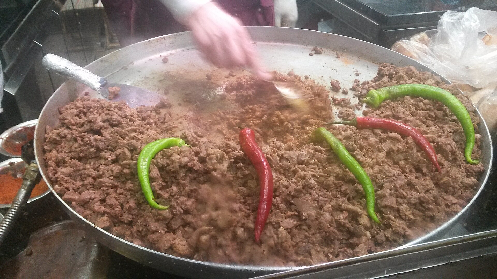 大きな浅い鉄鍋で炒める細切れ牛肉と青・赤の唐辛子、タントゥニの鍋