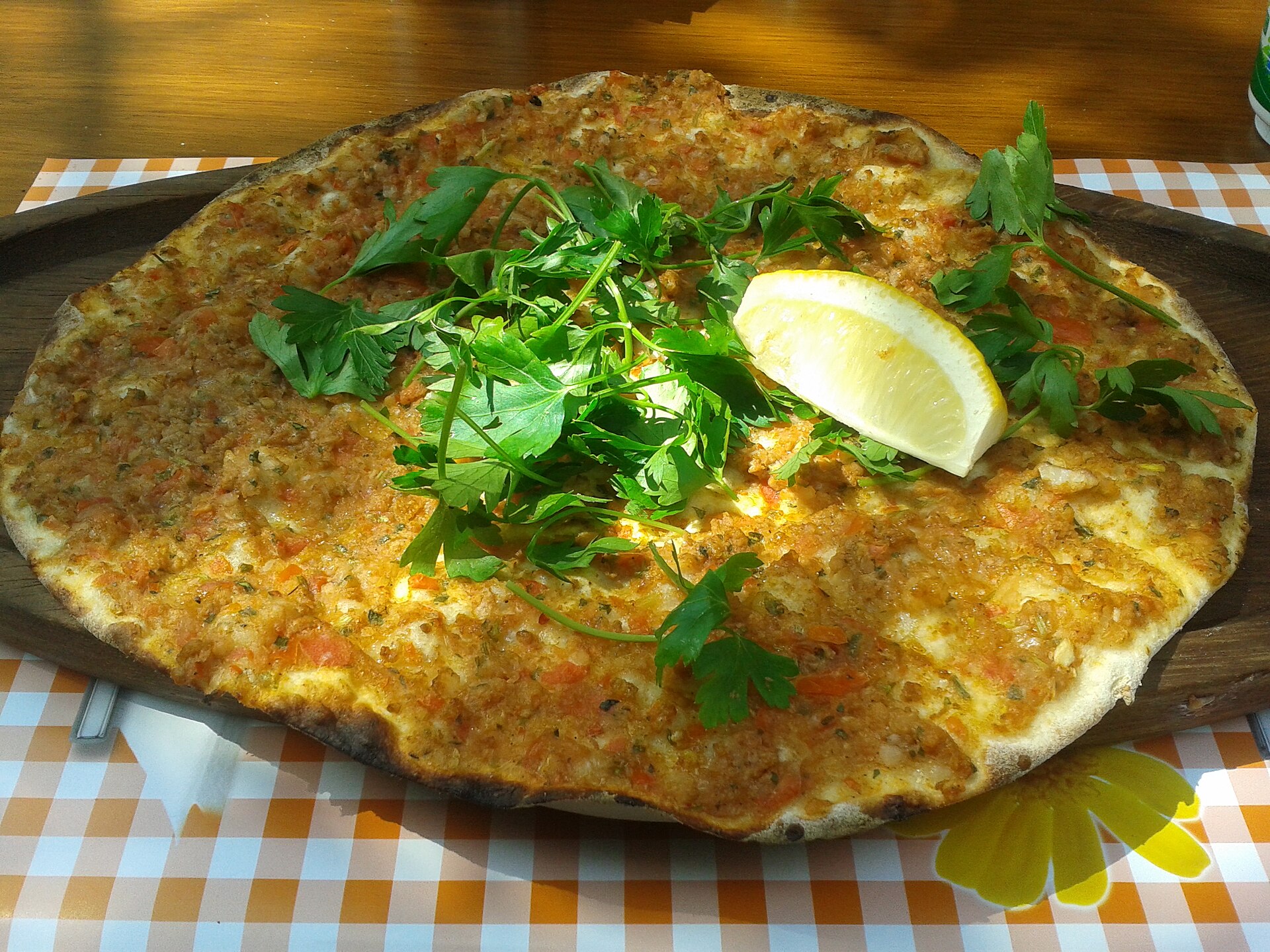 丸く薄い生地にひき肉を塗って焼いたラフマジュン、イタリアンパセリとレモン添え