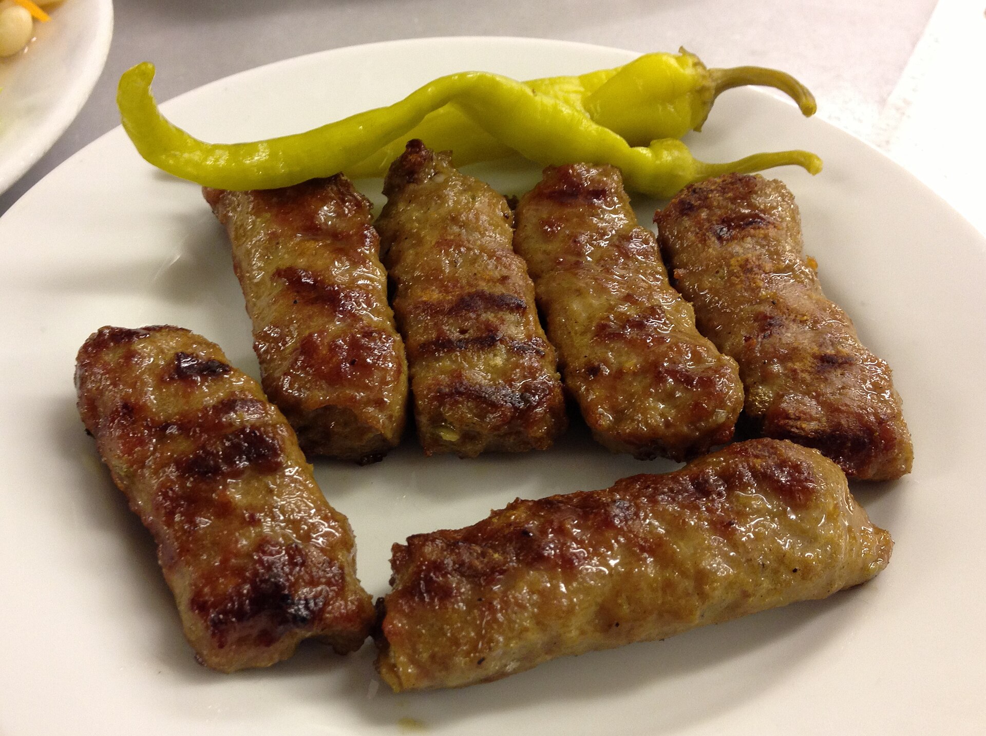 皿に並ぶ焼き目のついた細長いキョフテと青唐辛子の酢漬け