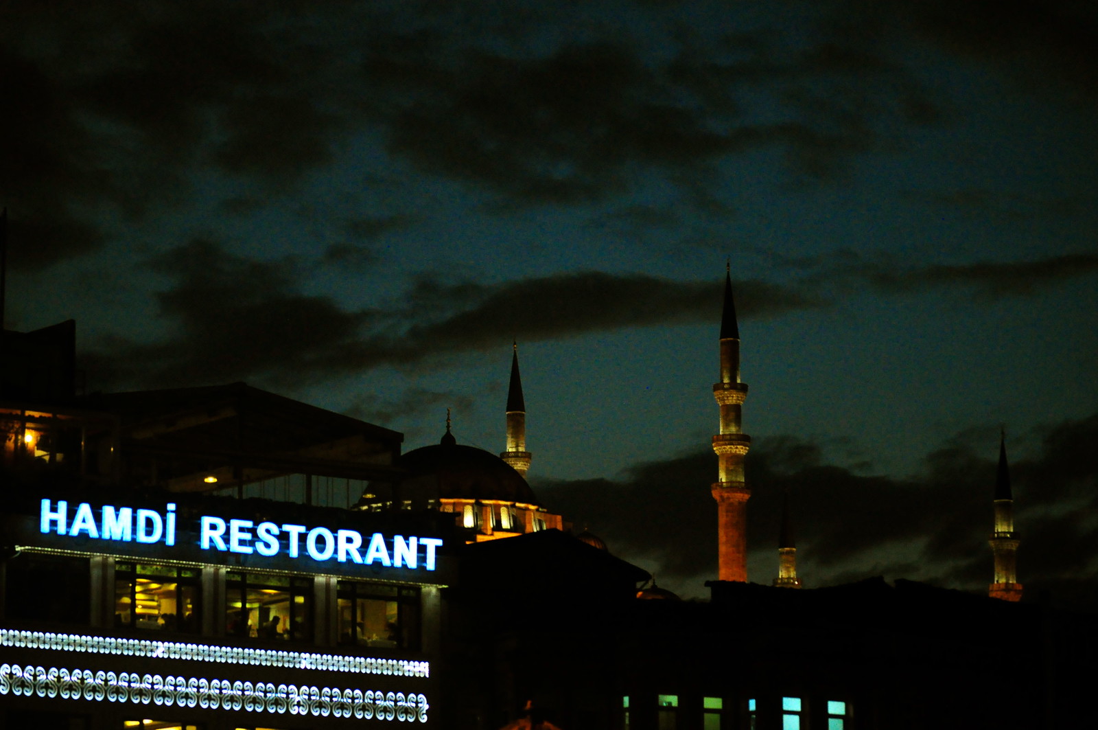 夜のエミノニュ、ネオンの「HAMDİ RESTORANT」の看板と奥にライトアップされたモスクのミナレット