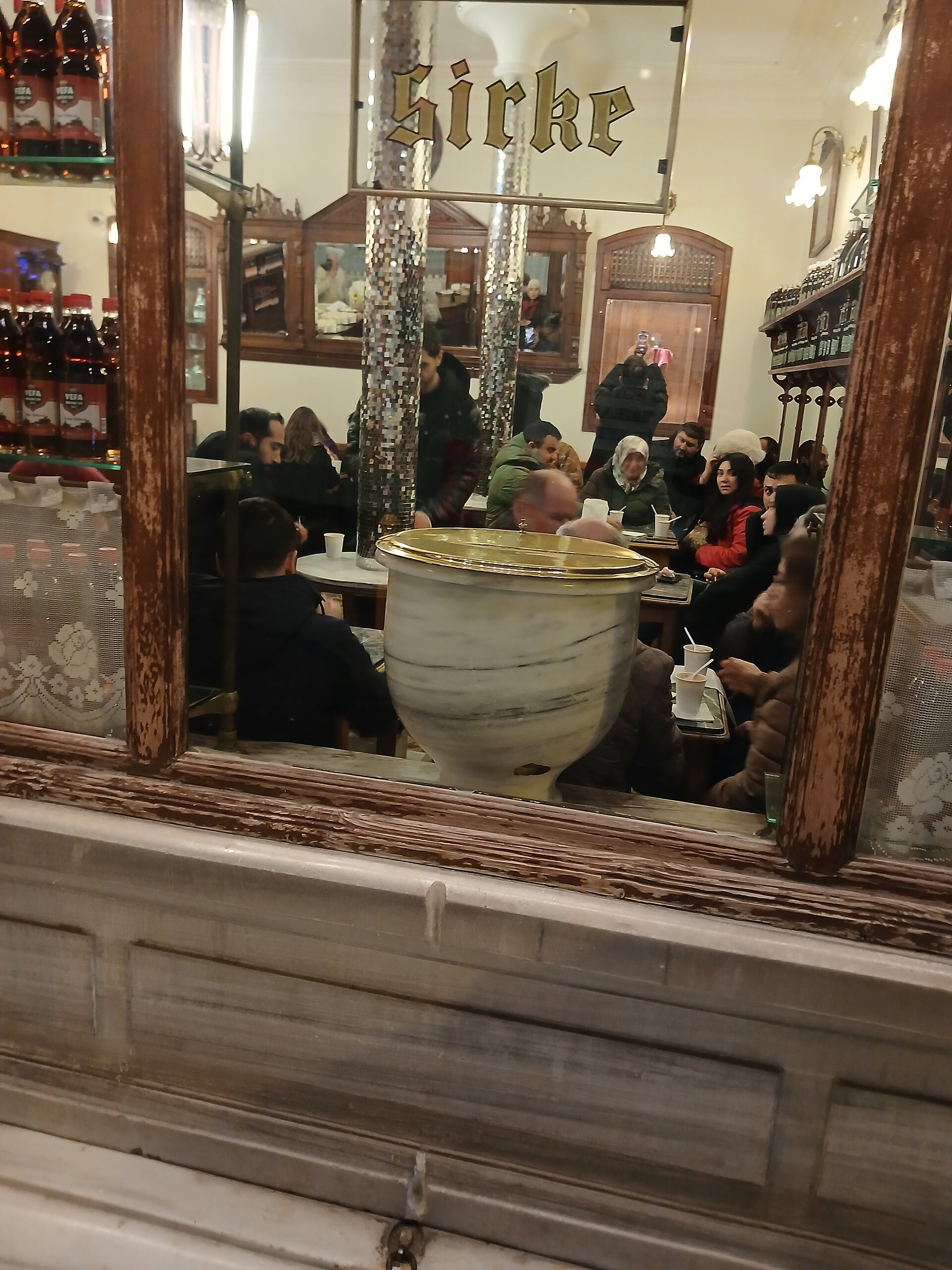 Vefa Bozacısı の店内、窓越しに見える大理石の台と真鍮の大きなボザの壺、壁の古い棚