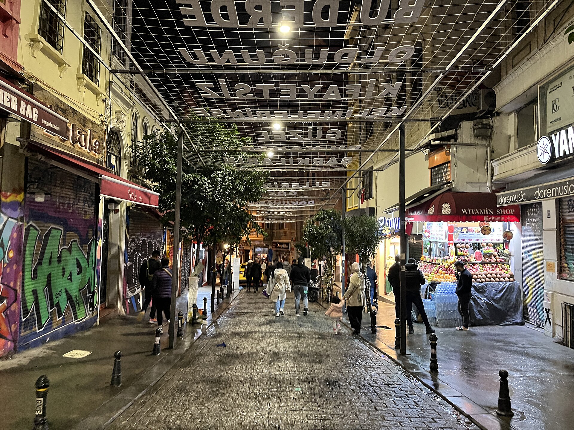 夜のベイオウルの石畳の路地、頭上の飾りと灯りのともる店