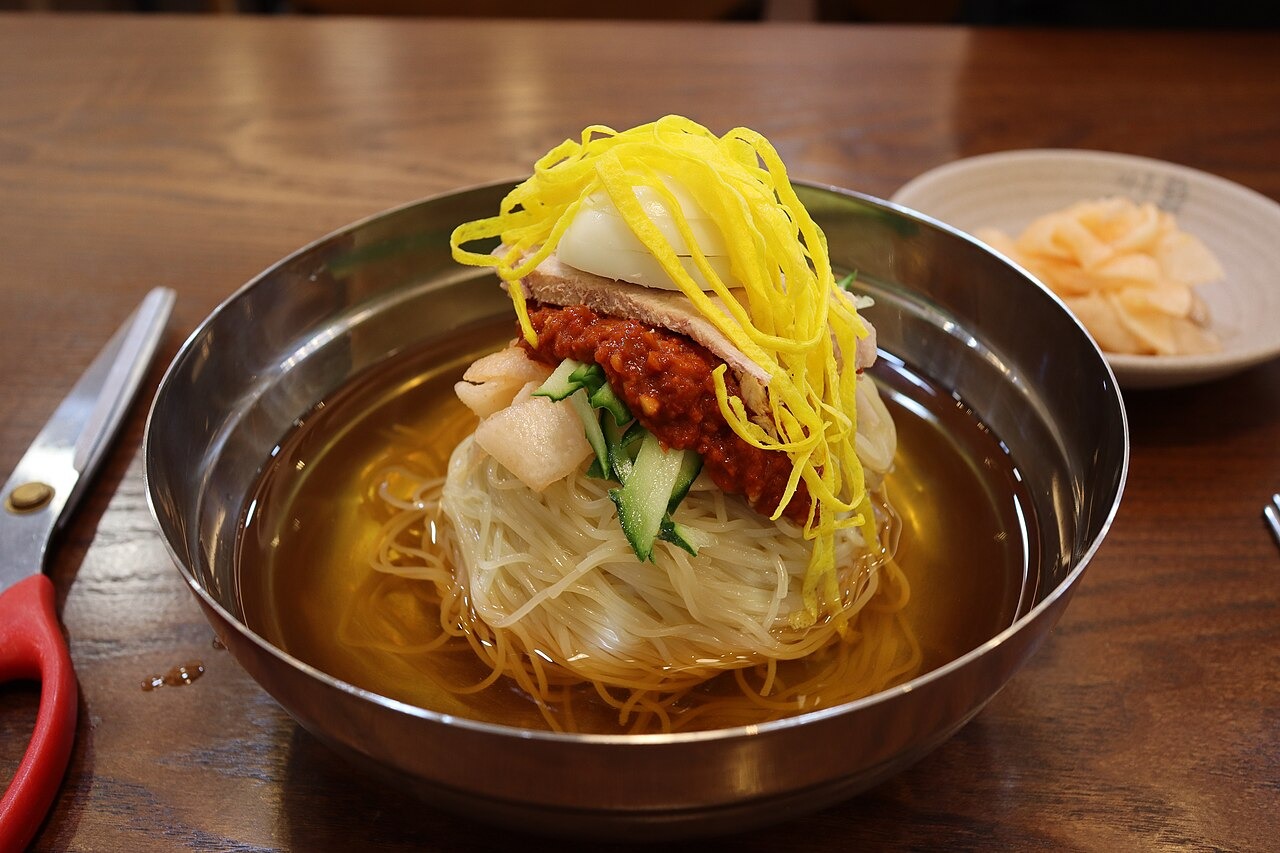 卵と赤い薬味をのせたミルミョン。持ち上げた麺の細さが見える。