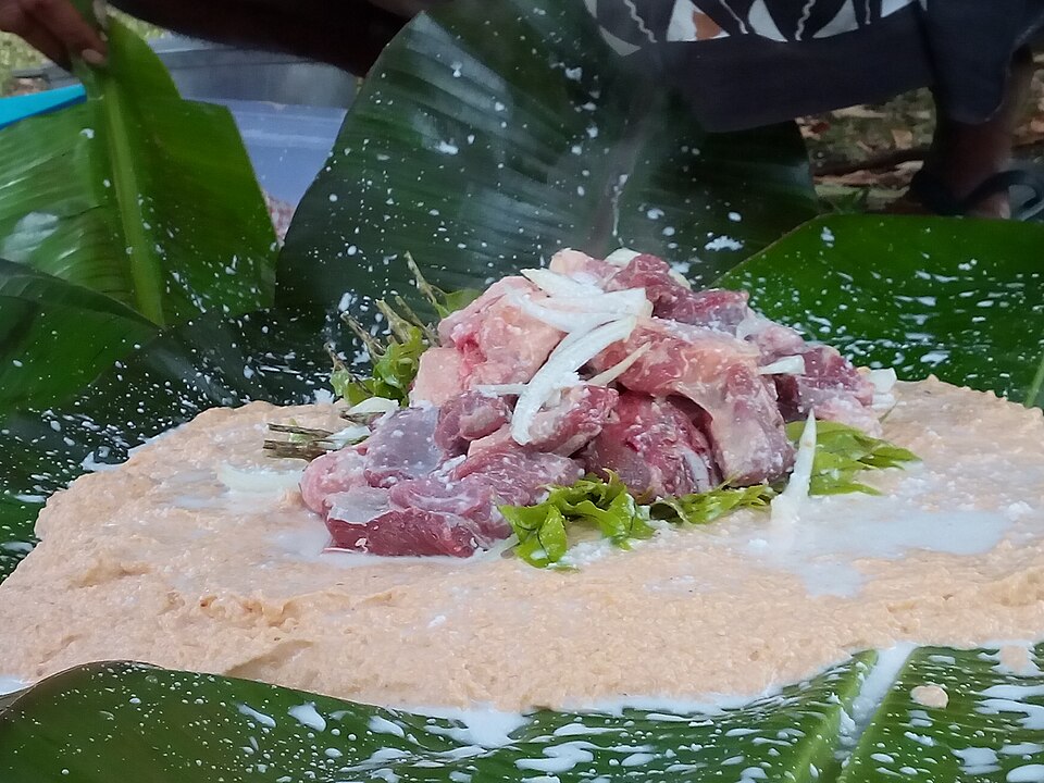葉の上に広げたすり下ろし生地に、切った肉と玉ねぎを載せたところ
