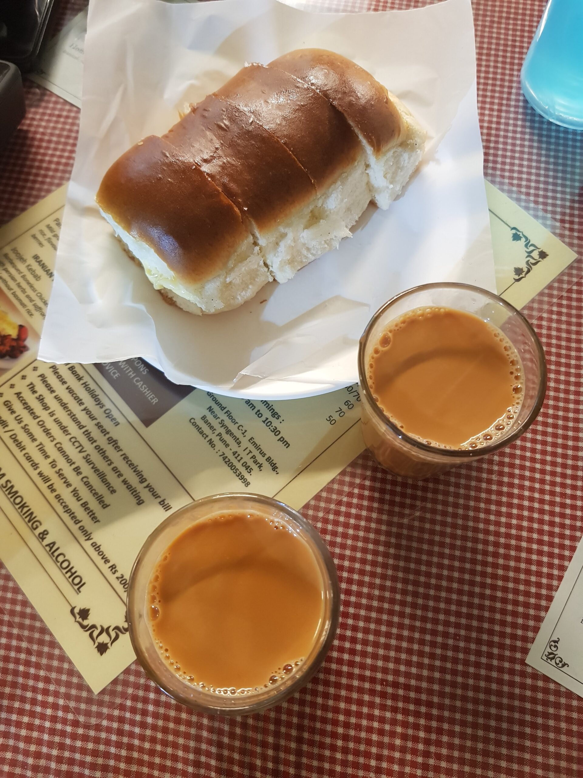 白い紙に載ったバターを塗ったバン（バン・マスカ）とグラス2杯のチャイ