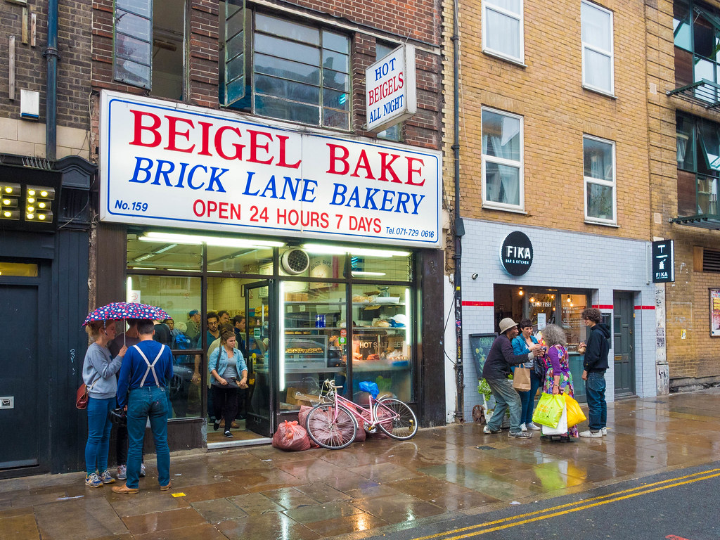 雨に濡れた歩道とベイゲル・ベイクの店先。「BEIGEL BAKE BRICK LANE BAKERY OPEN 24 HOURS 7 DAYS」の看板