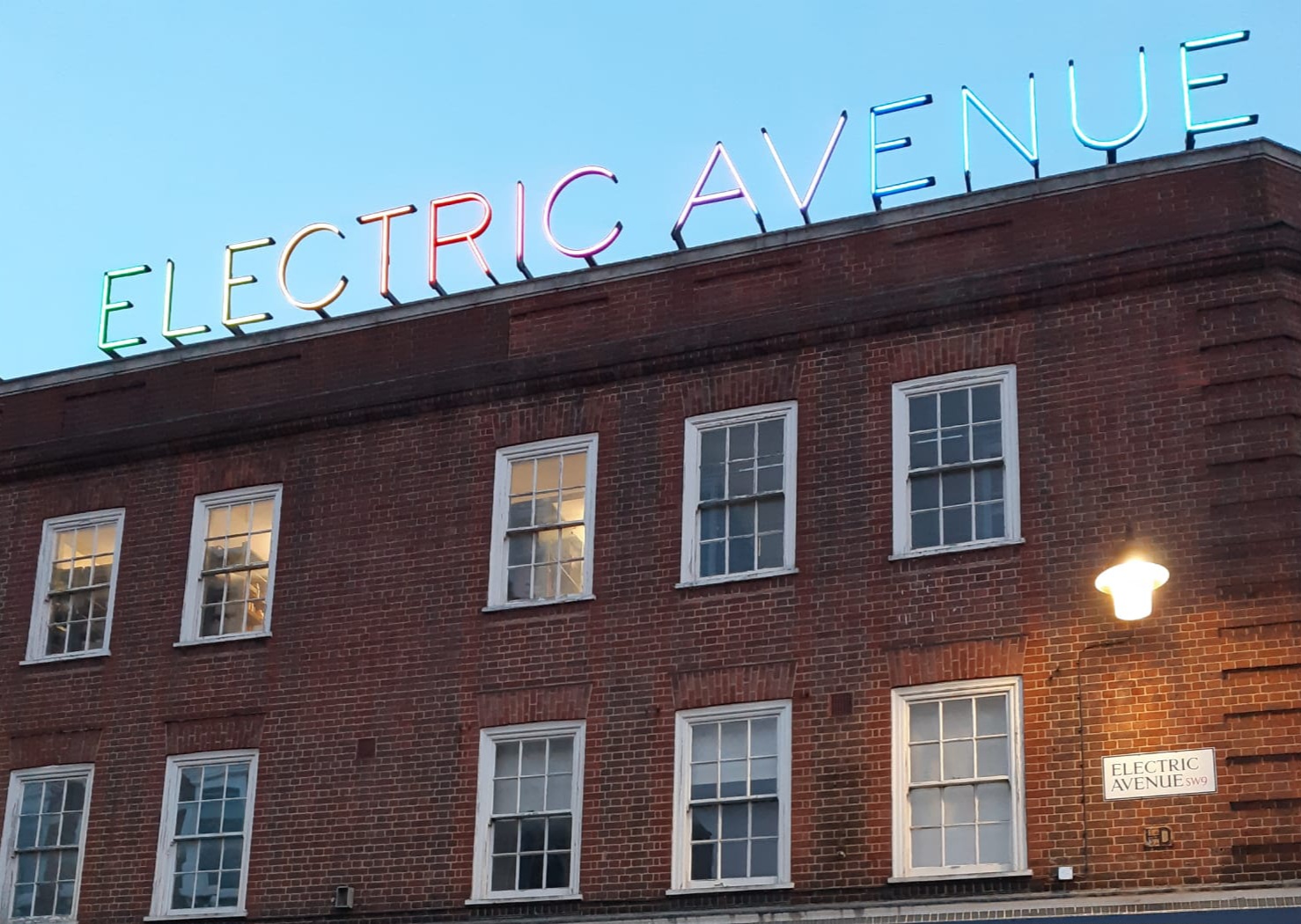 赤レンガの建物の上に「ELECTRIC AVENUE」のネオン文字、青空