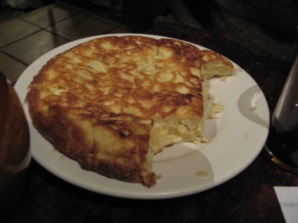 白い皿の焼き色のついた丸いトルティージャ。一部が切り取られている