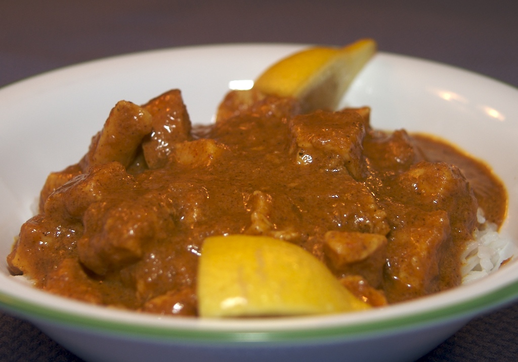 白い器に盛った赤茶色のチキンカレーとレモン