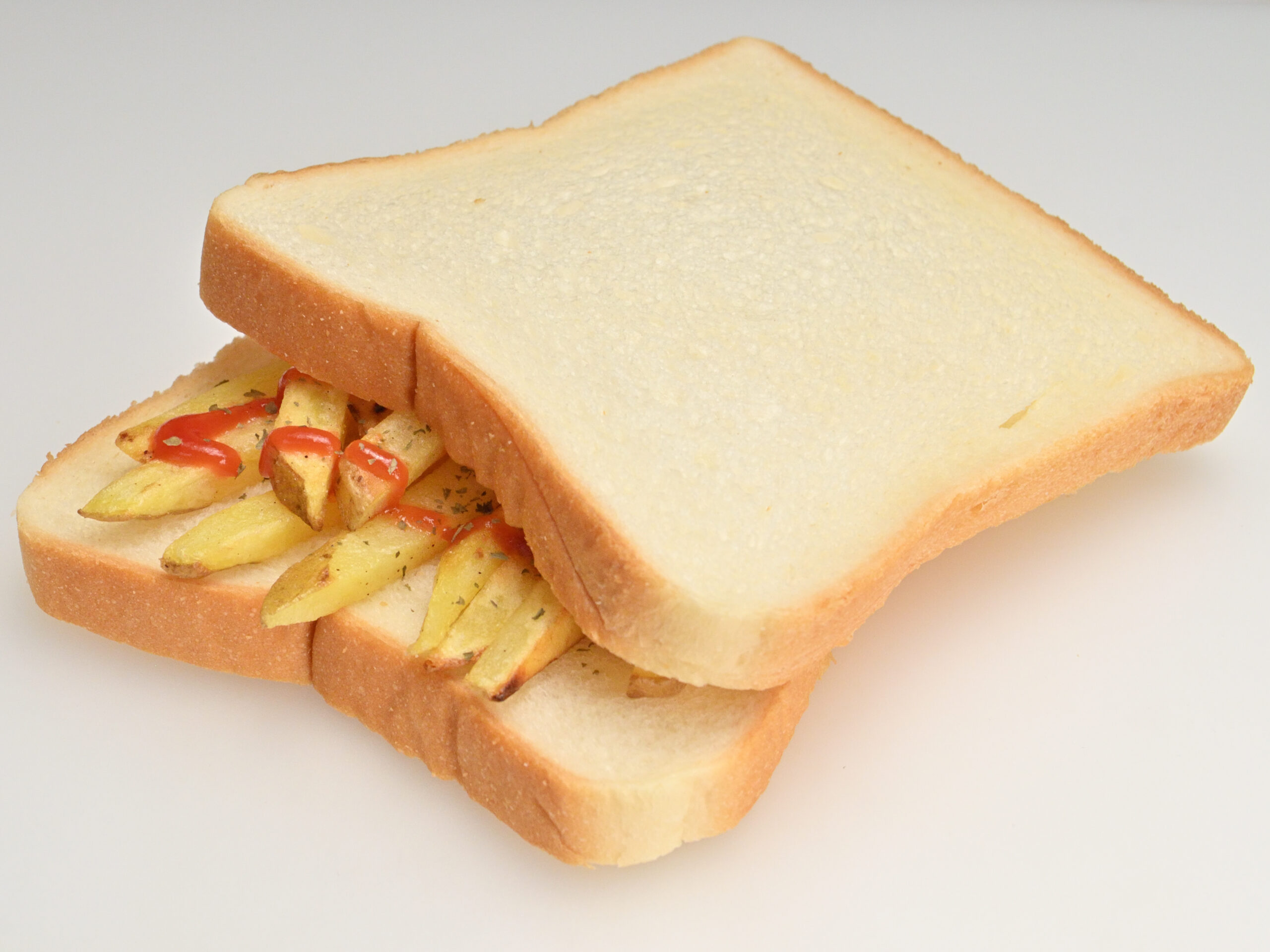 白い食パン2枚にケチャップをかけたチップス（フライドポテト）を挟んだサンドイッチ