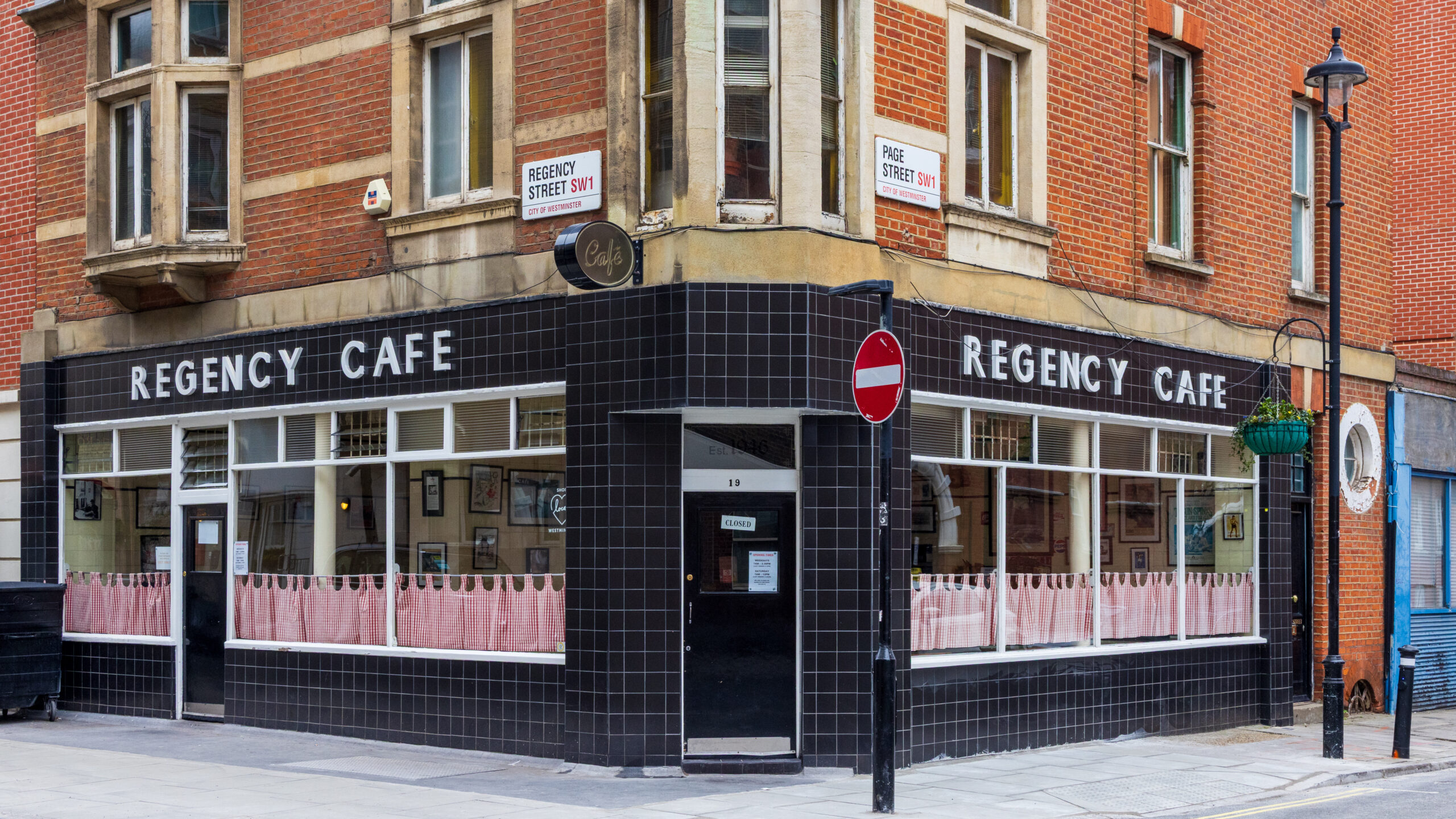 黒いタイル張りの外壁に白い「REGENCY CAFE」の文字、赤れんがの建物の角