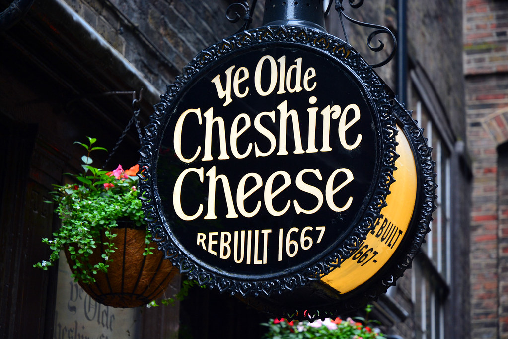 「Ye Olde Cheshire Cheese REBUILT 1667」の黒い円形の吊り看板と花のハンギングバスケット
