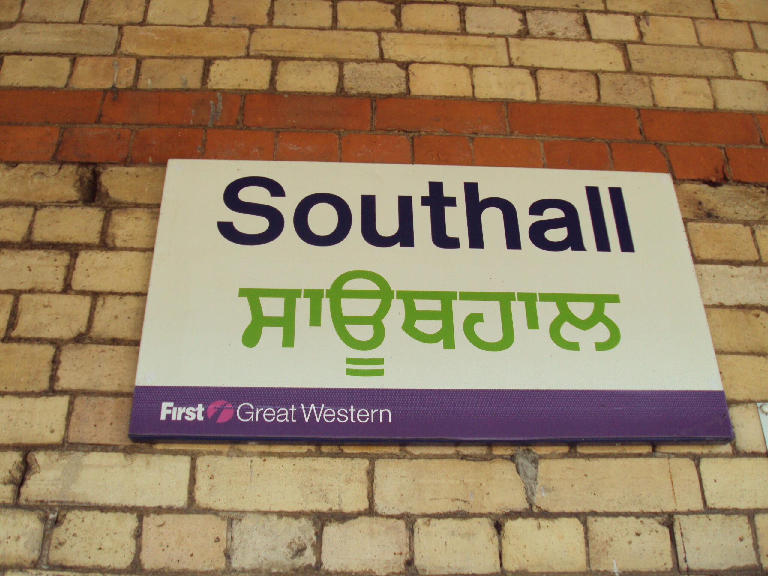 黄色いれんが壁に掛かった駅名板。英語「Southall」とグルムキー文字のパンジャーブ語を併記