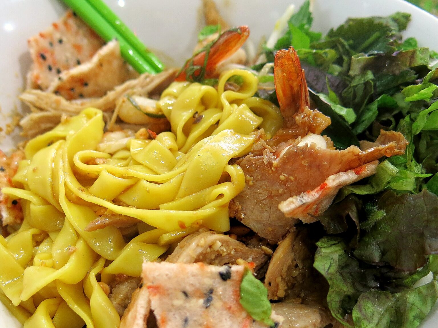 黄色く染めた平たい麺、海老、練りもの、豚肉、生野菜がたっぷりのった一杯
