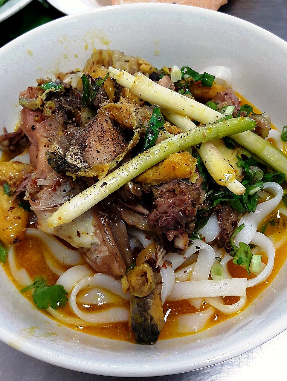 白い丼に平たい麺とほぐした魚の身、レモングラスの茎、黒こしょう