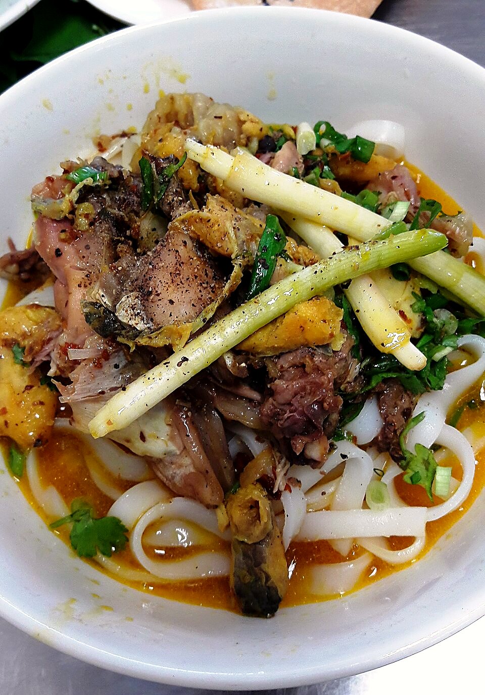 白い丼に平たい麺、ほぐした魚、レモングラスの茎、香草