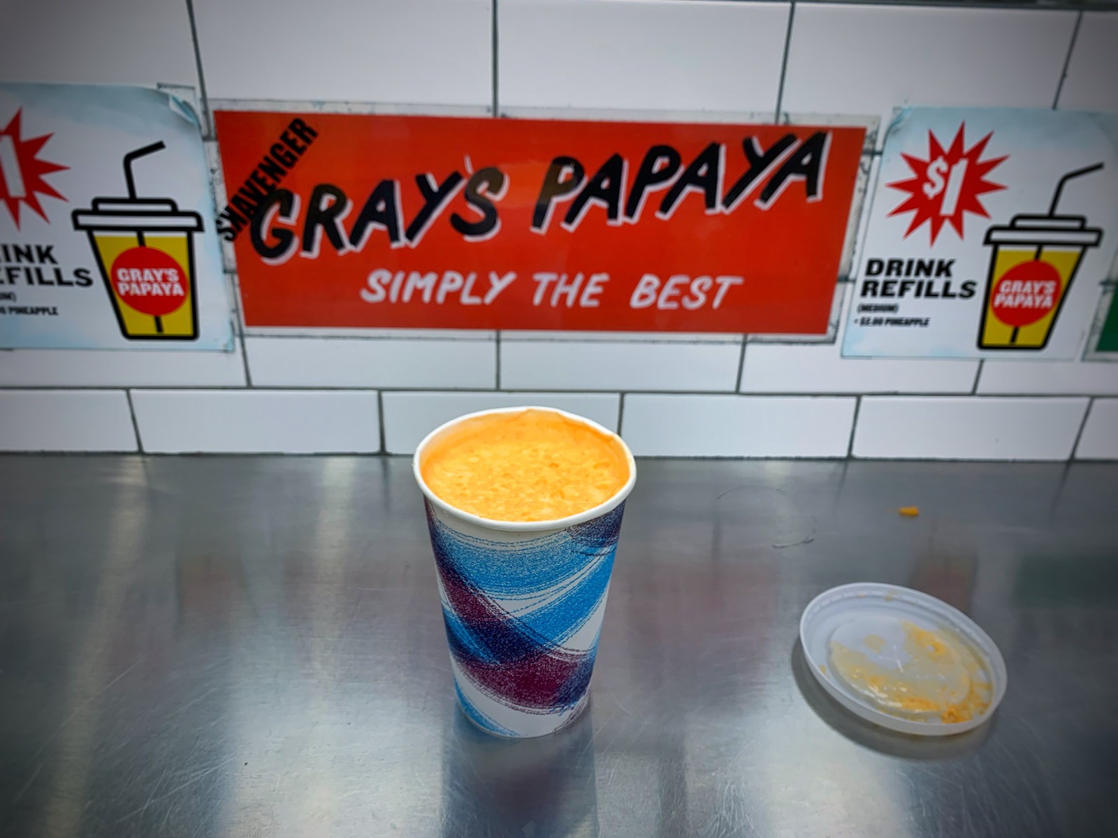 Gray's Papaya のカウンターに置いた紙コップのパパイヤ・ドリンク、背後に店の看板