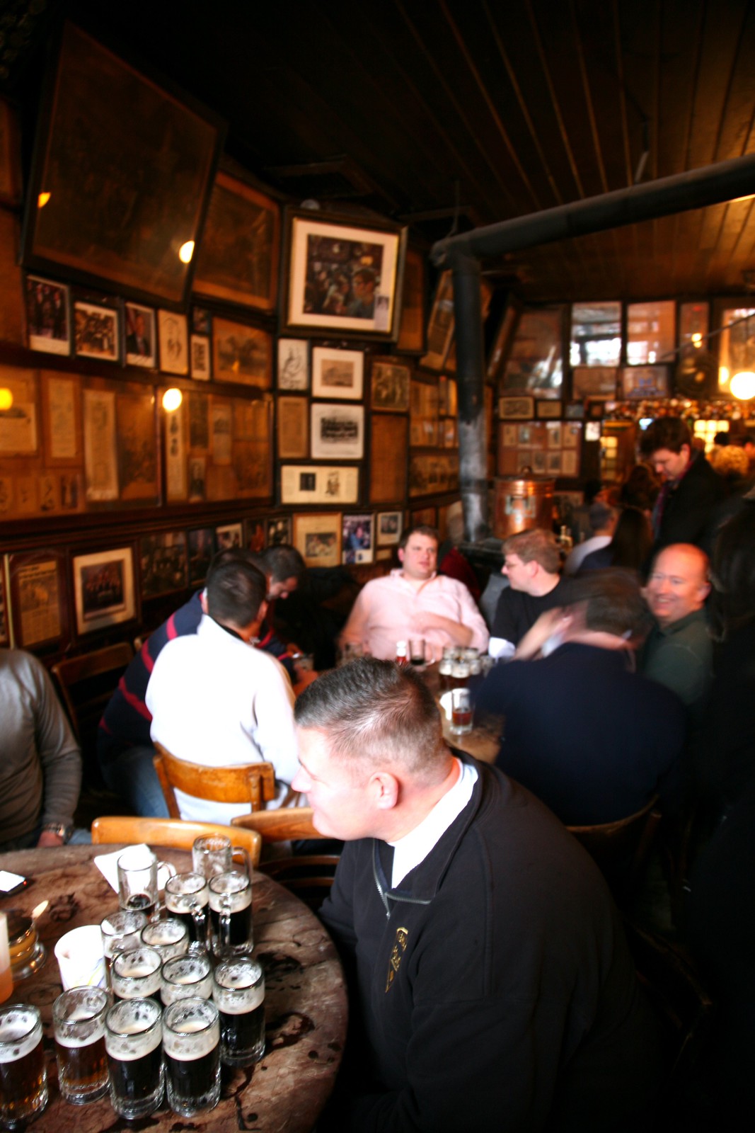 McSorley's の丸テーブルに並ぶ小さなジョッキのエール、壁一面の額