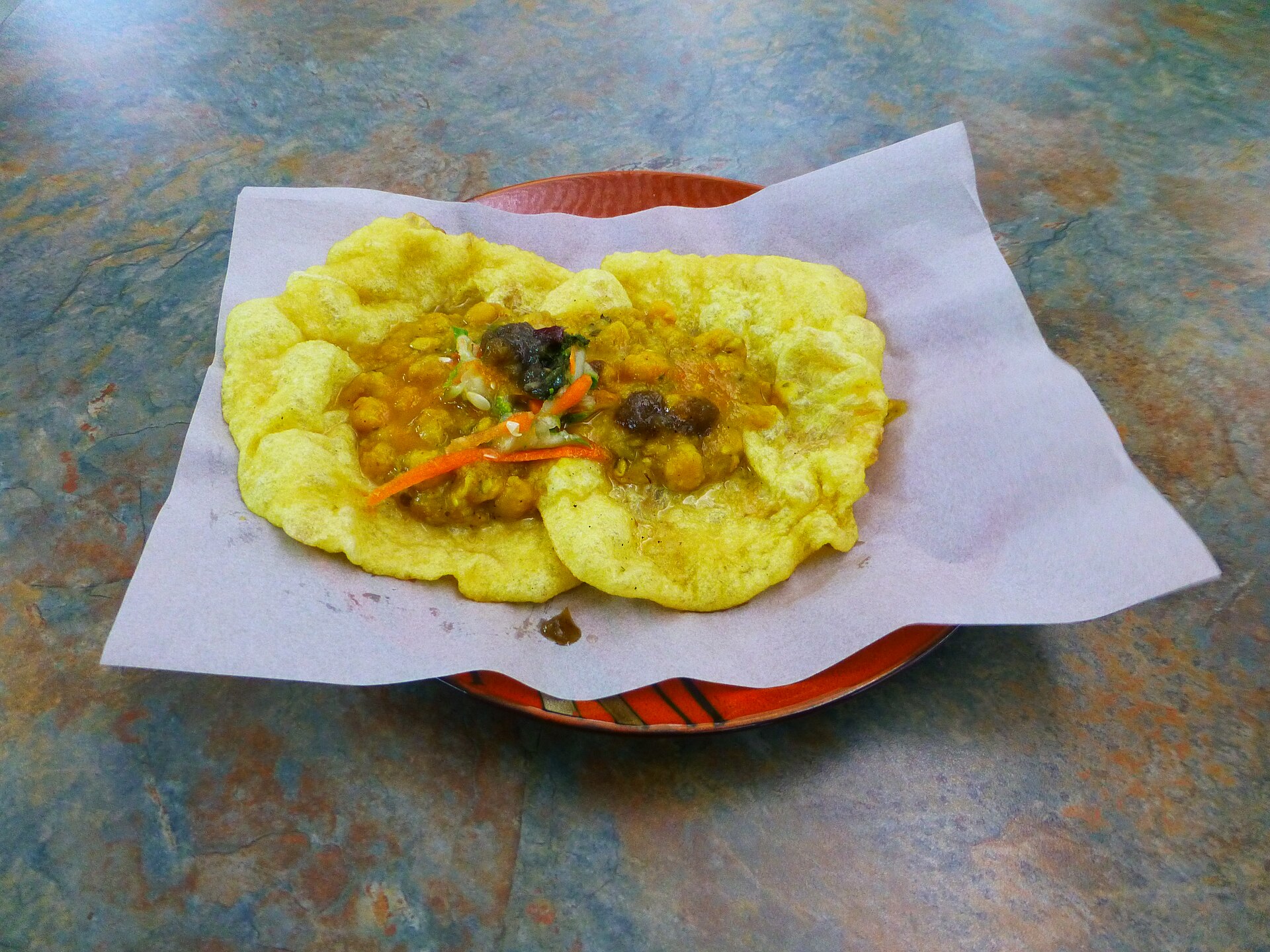 紙に載せたダブルス。黄色い揚げパンにカレー味のひよこ豆とソース