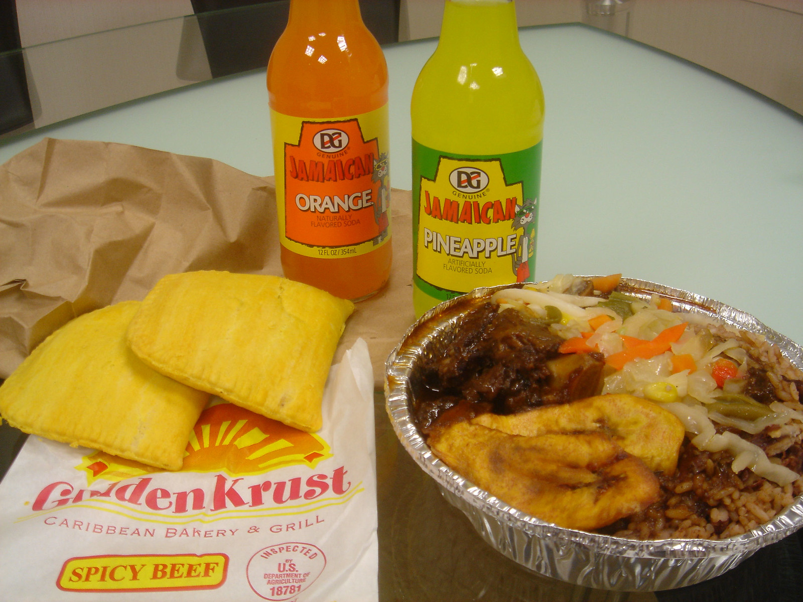 Golden Krust の紙袋の上に置いたビーフパティ2枚とジャーク料理、ジャマイカの瓶ソーダ