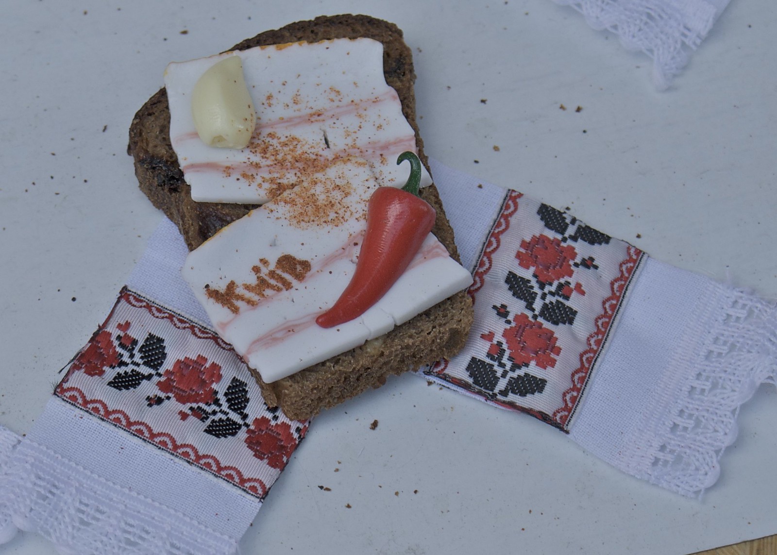 黒パンにのせた白いサロの薄切り、赤唐辛子とにんにく、刺繍のナプキン