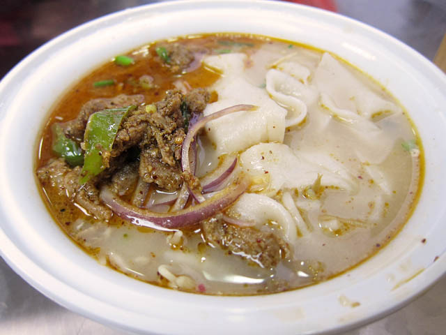 発泡容器に入ったスープ仕立ての幅広の手延べ麺、クミン風味のラム肉と赤玉ねぎ、青唐辛子