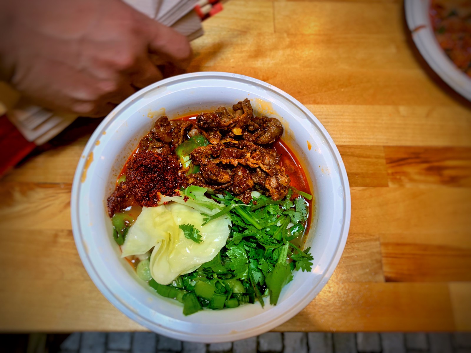木のテーブルの器に、辣油の効いたラム肉と香菜をのせた手延べ麺